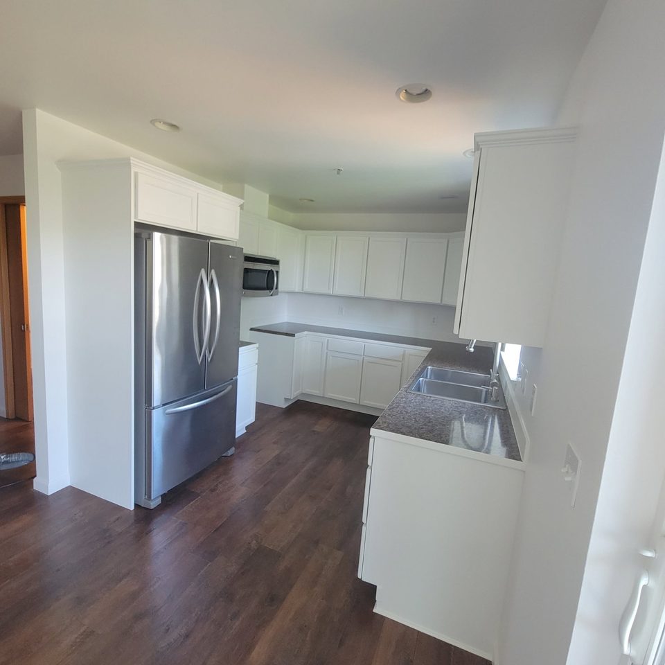 White kitchen interior from the entry with dark flooring.