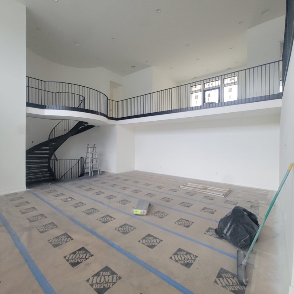 Curved staircase with dark railings, white walls and protected flooring.