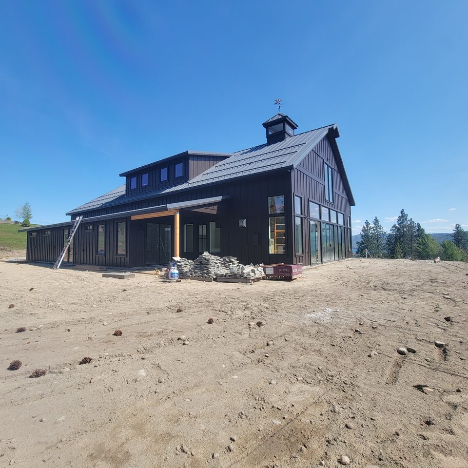 Dark board-and-batten building with a gabled roof, a cupola and wood porch posts.