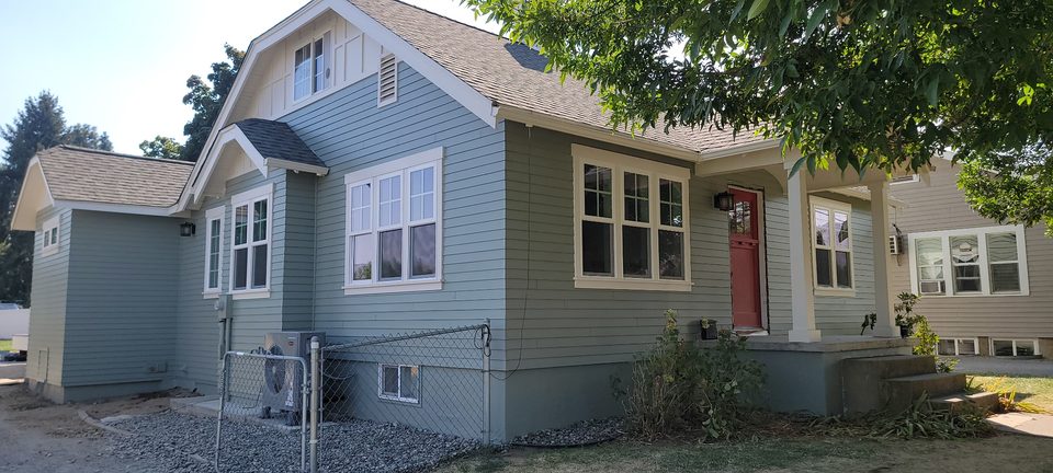 Front view of a green house with light trim.